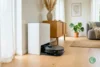 Robot vacuum docking station in a modern living room showing full-service base with robot returning to dock